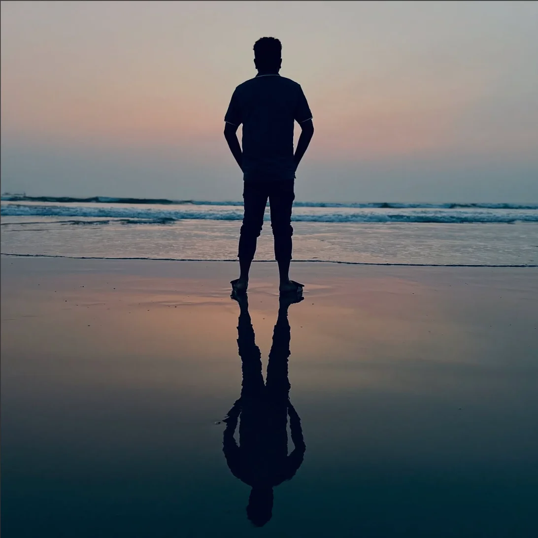 Silhouette standing on a wet beach at sunset, reflected in the sand